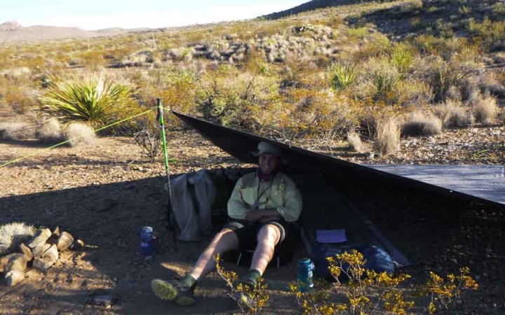 a gap year student sits under a tarp shelter in the desert while on an outward bound course
